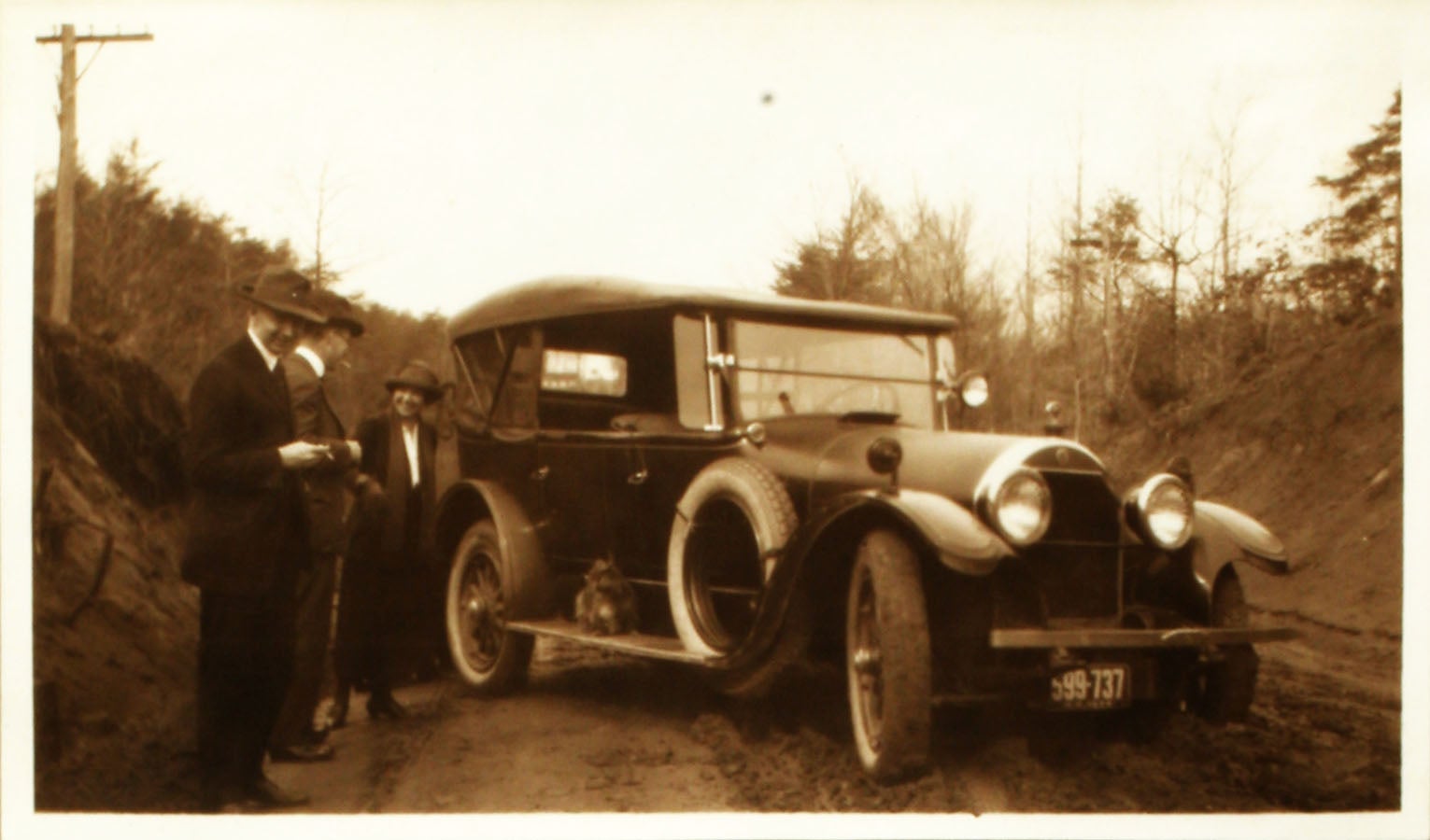 archival photo of two men and woman standing alongside car