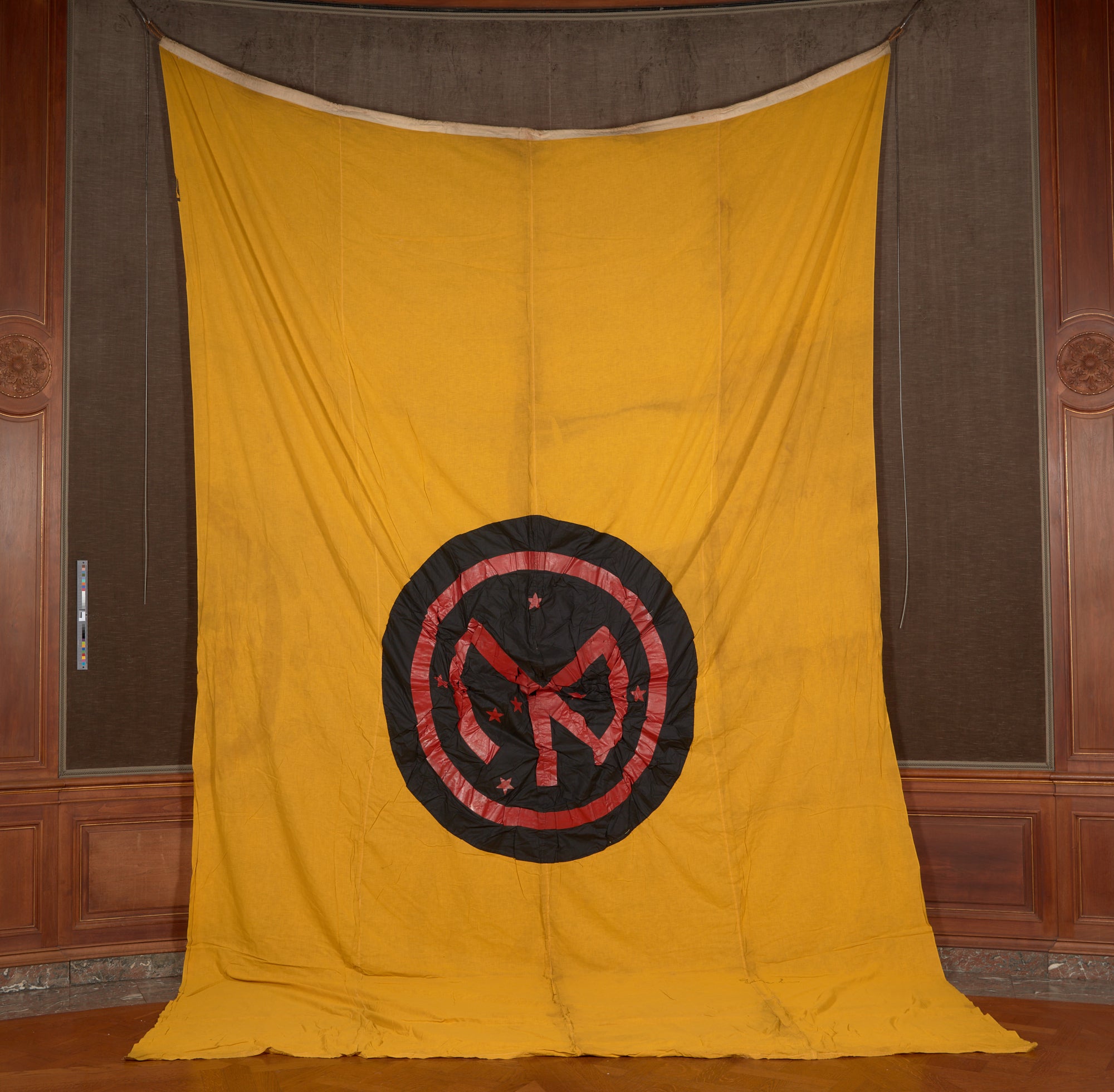 A yellow banner hanging vertically with the insignia of the 27th Infantry Division at its center