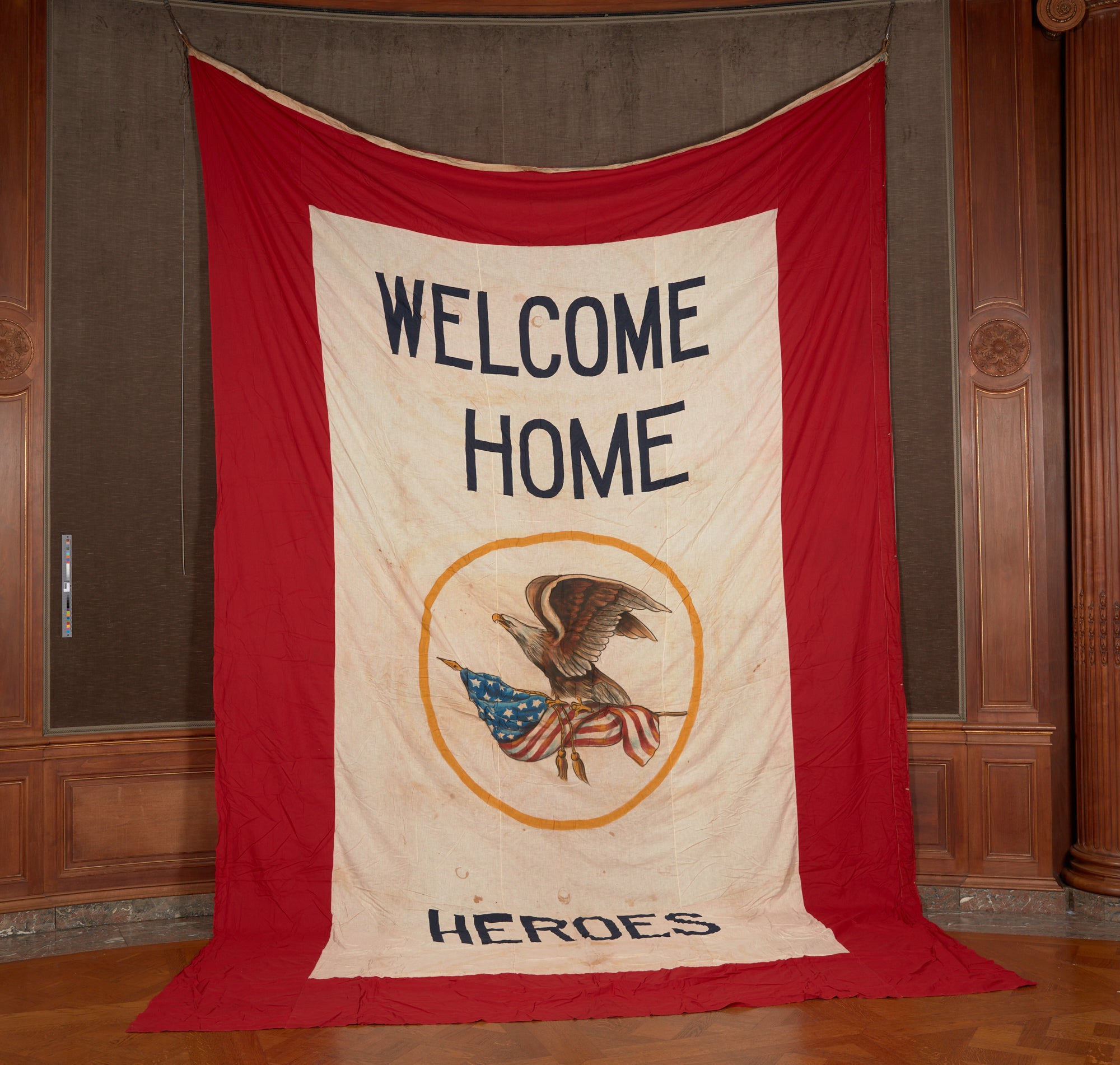 A large white banner with red border with the words "Welcome Home Heroes" and an insignia at the center featuring an eagle carrying an American flag