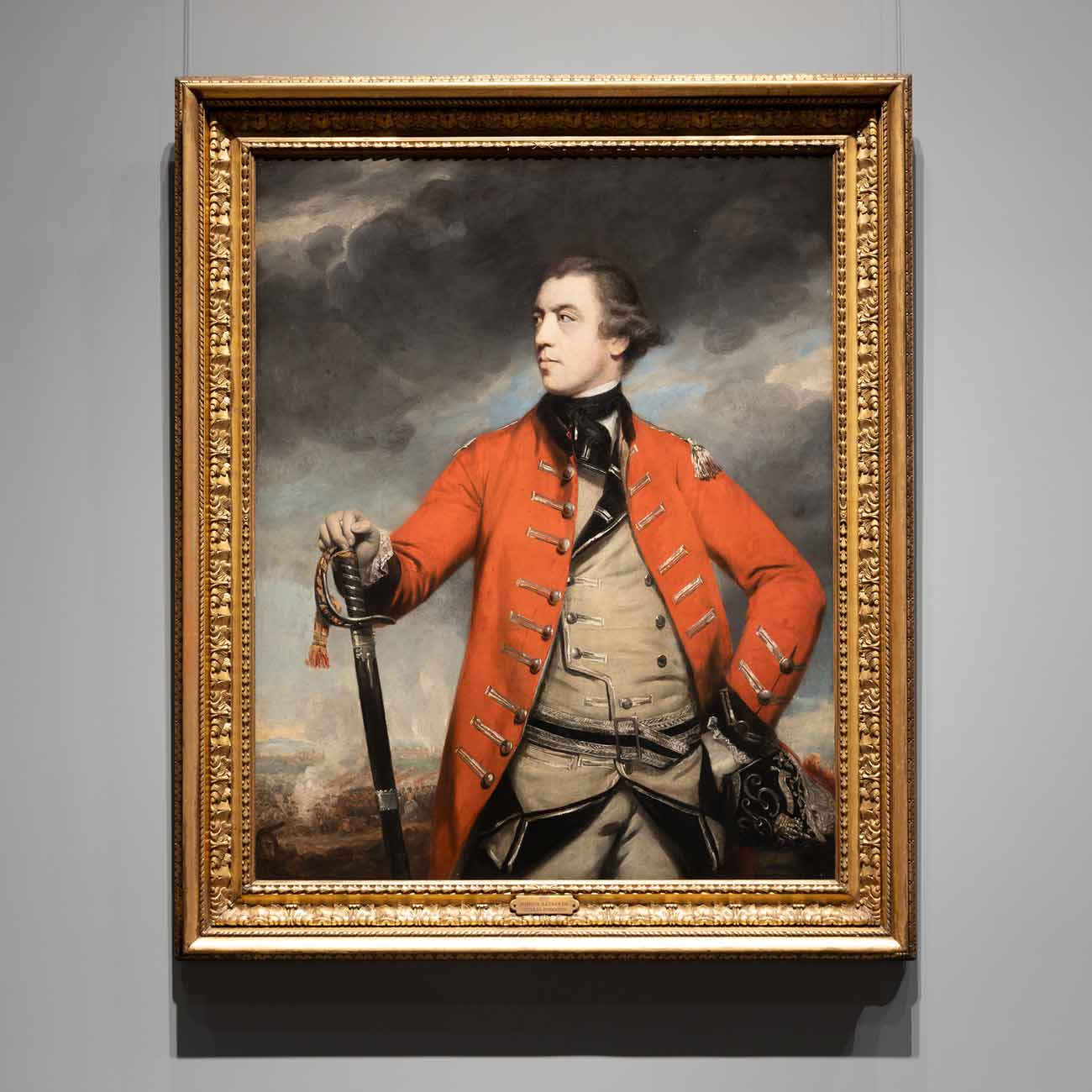 Framed painting of a confident British general in a red coat against a stormy backdrop with soldiers in the distance