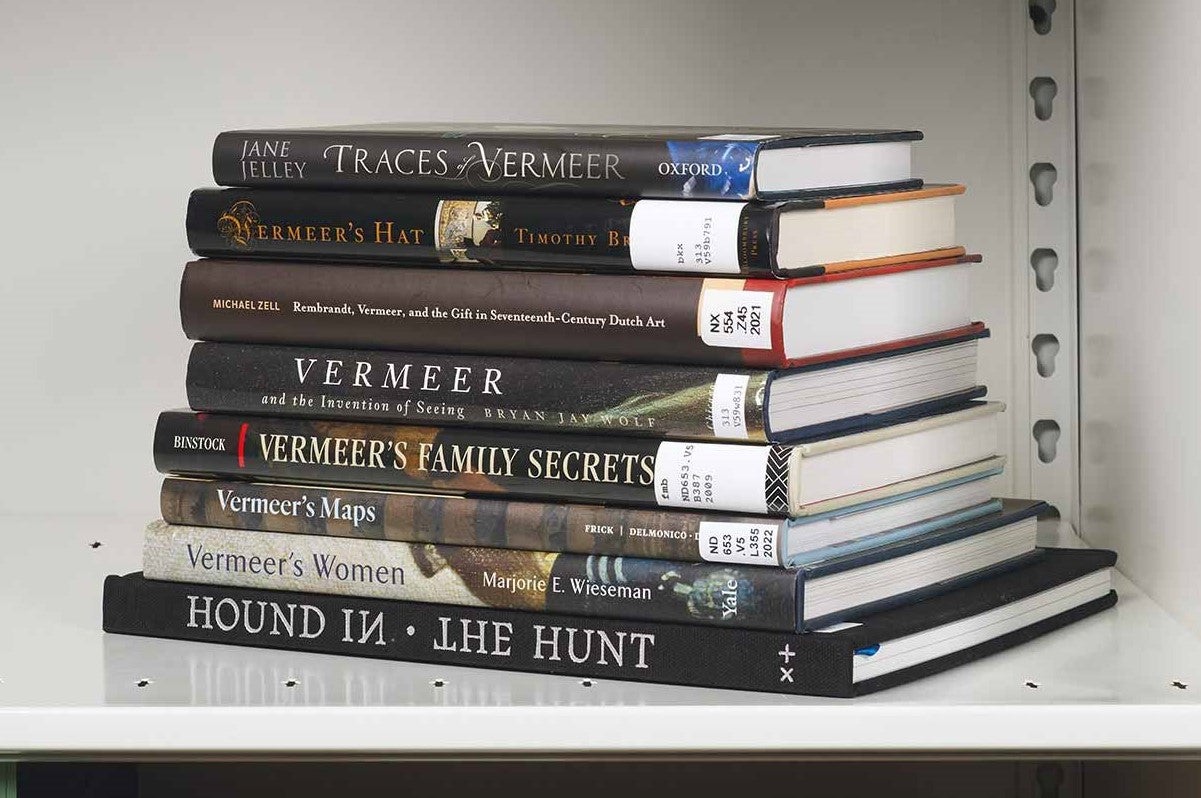 Stack of eight books about Vermeer on a white shelf