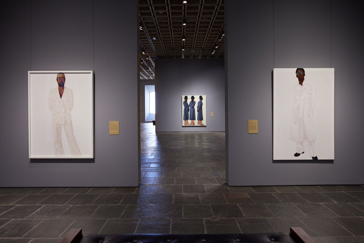 Two white-on-white portraits of men flanking a triple portrait of a man in a long blue coat in a gallery beyond