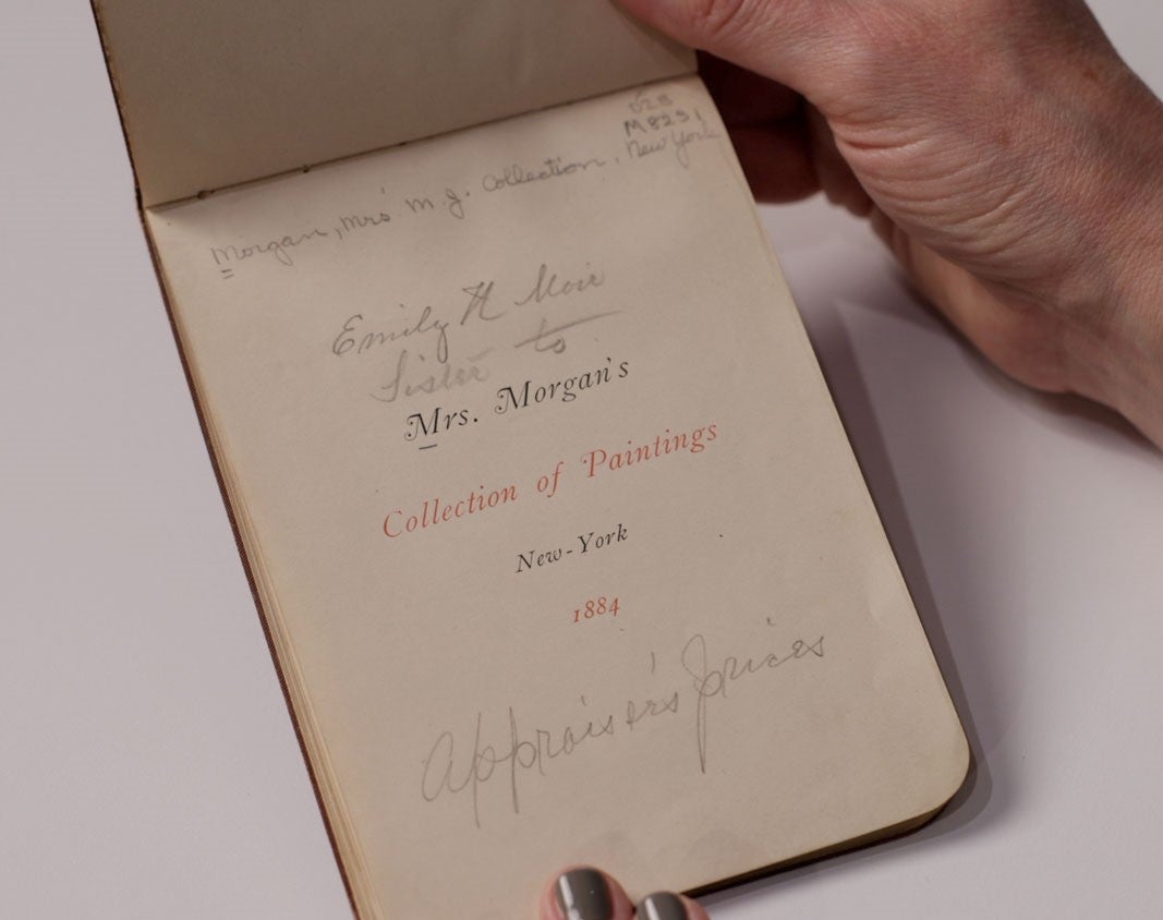 Hands holding a small guidebook with the title "Mrs. Morgan's Collection of Paintings, New York, 1884"
