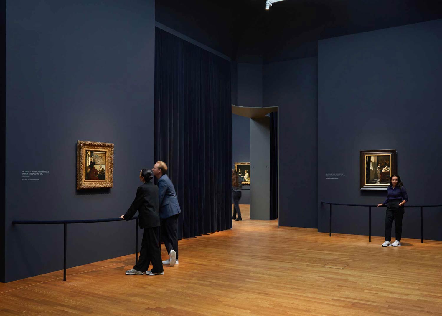 Visitors looking at paintings hanging in a gallery with blue walls
