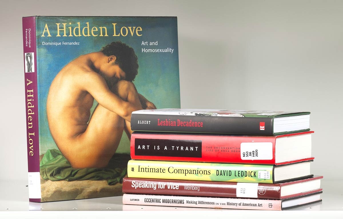 Book stack next to a book cover entitled "A Hidden Love" featuring an artwork of a nude male figure crouched on the ground