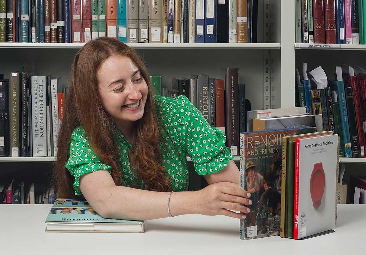 Woman in a green shirt picking a book from a stack of books on a table