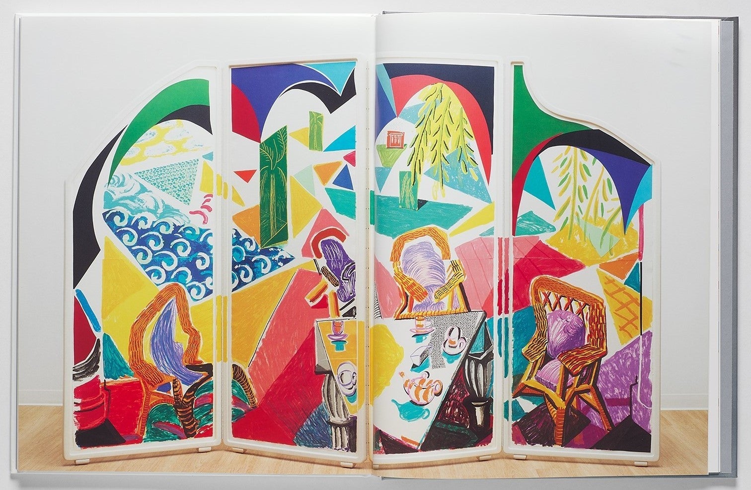 Book spread showing a folding screen painted with a colorful stylized scene of a table set for tea overlooking the ocean and trees