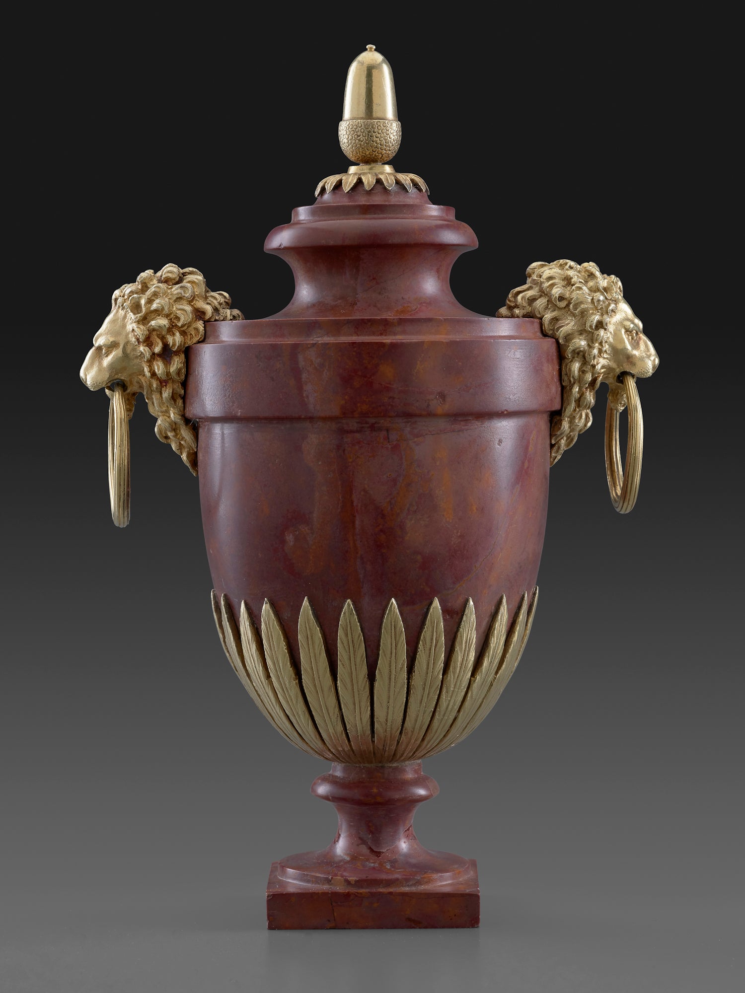 an ovoid blood-red marble vase adorned with gilt-silver lanceolate leaves and the heads of two lions with rings in their jaws