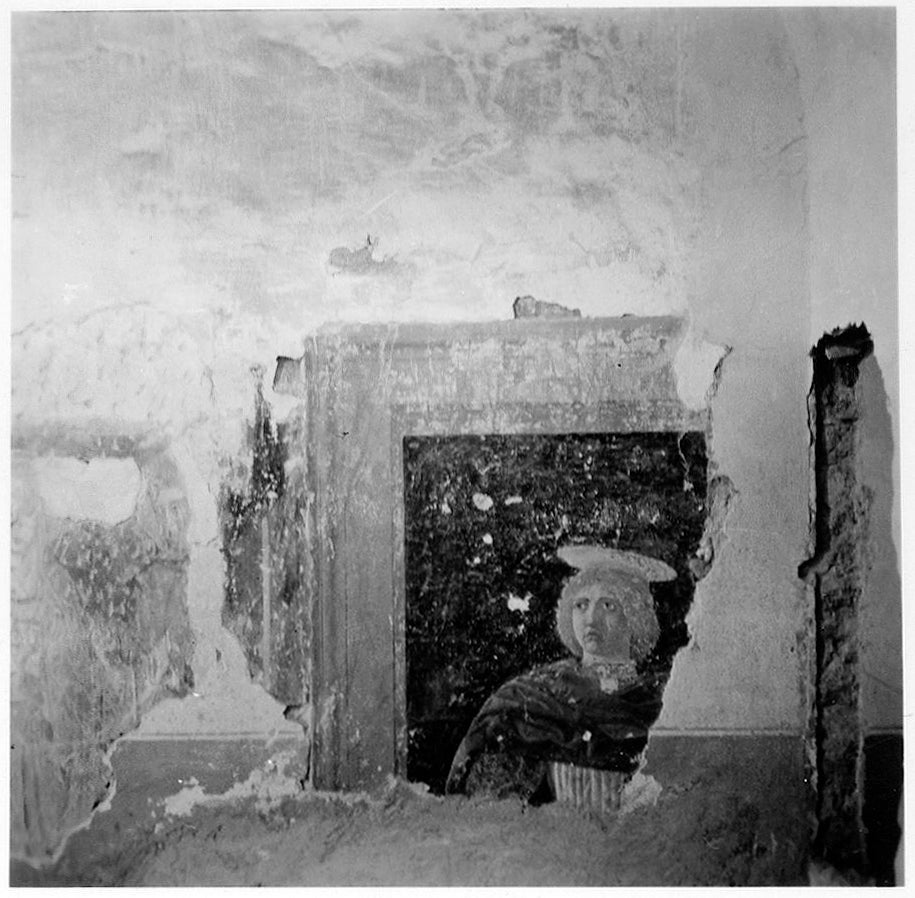 Corner of a room with a section of fresco depicting the head and shoulders of a young blond man.