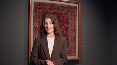 video still of woman standing in front of carpet on wall in gallery