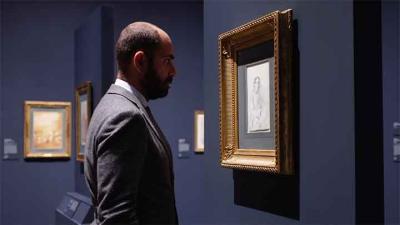 video still of Xavier F. Salomon looking closely at work in gallery