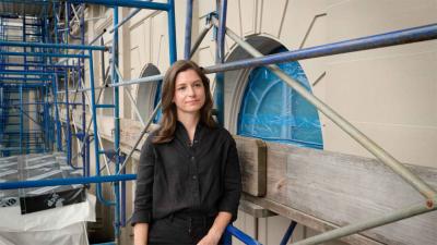 woman, Lizzie Olson, standing in front of building facade and scaffolding