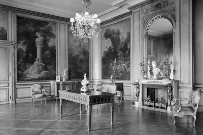 photo of room with paintings in panels, table in center, lighting fixture, circa 1927