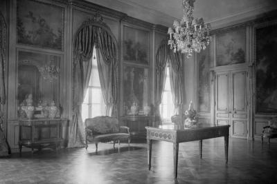 photo of room with paintings in panels, table in center, urns on tables, lighting fixture, circa 1927