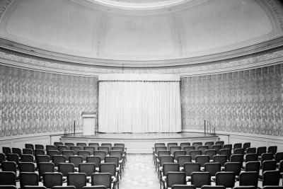 photo of dome-like room with empty chairs, stage and curtain, circa 1966
