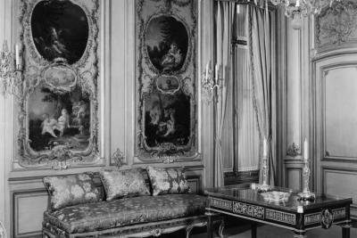 photo of room with couch, table, paintings in panels, chandelier, circa 1940
