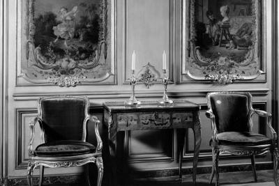 photo of room with chairs with paintings in panels and table with cancles, circa 1940