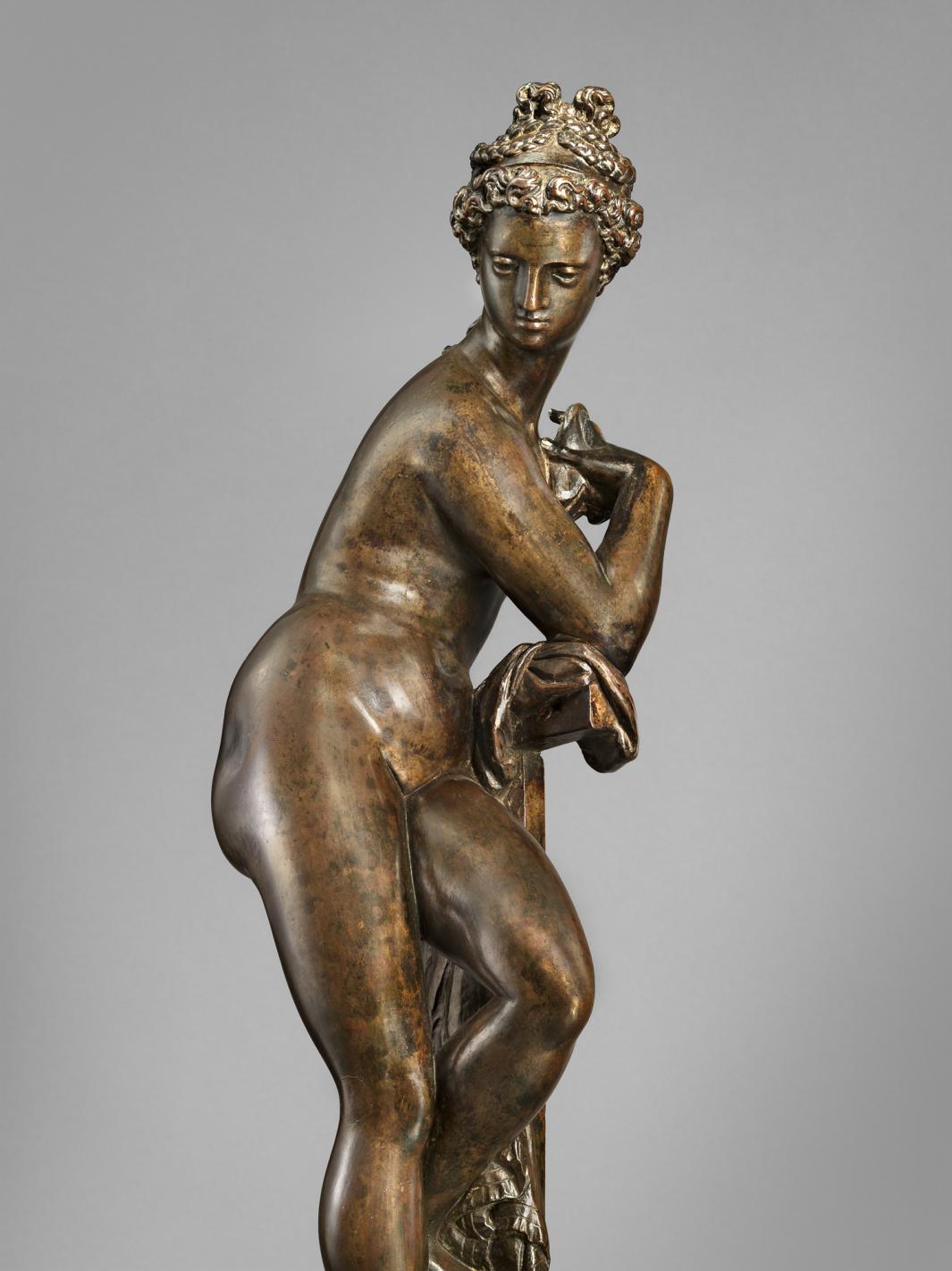 Bronze sculpture of a standing woman, leaning on a post, side view.