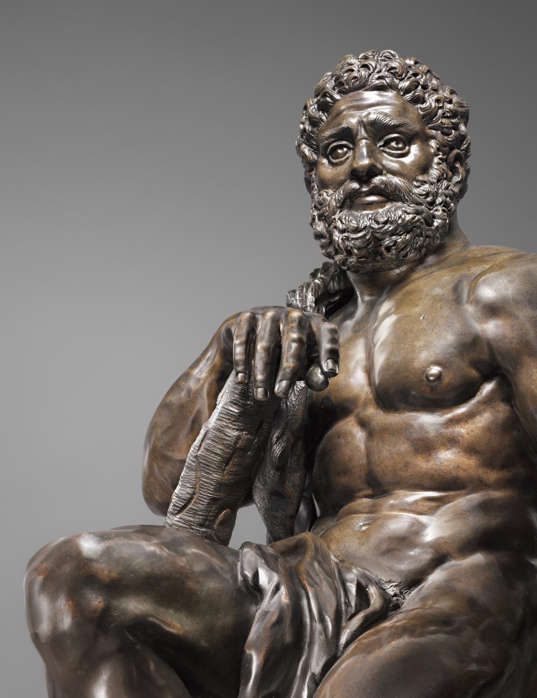 Bronze sculpture of seated male figure with a club, detail of face.  