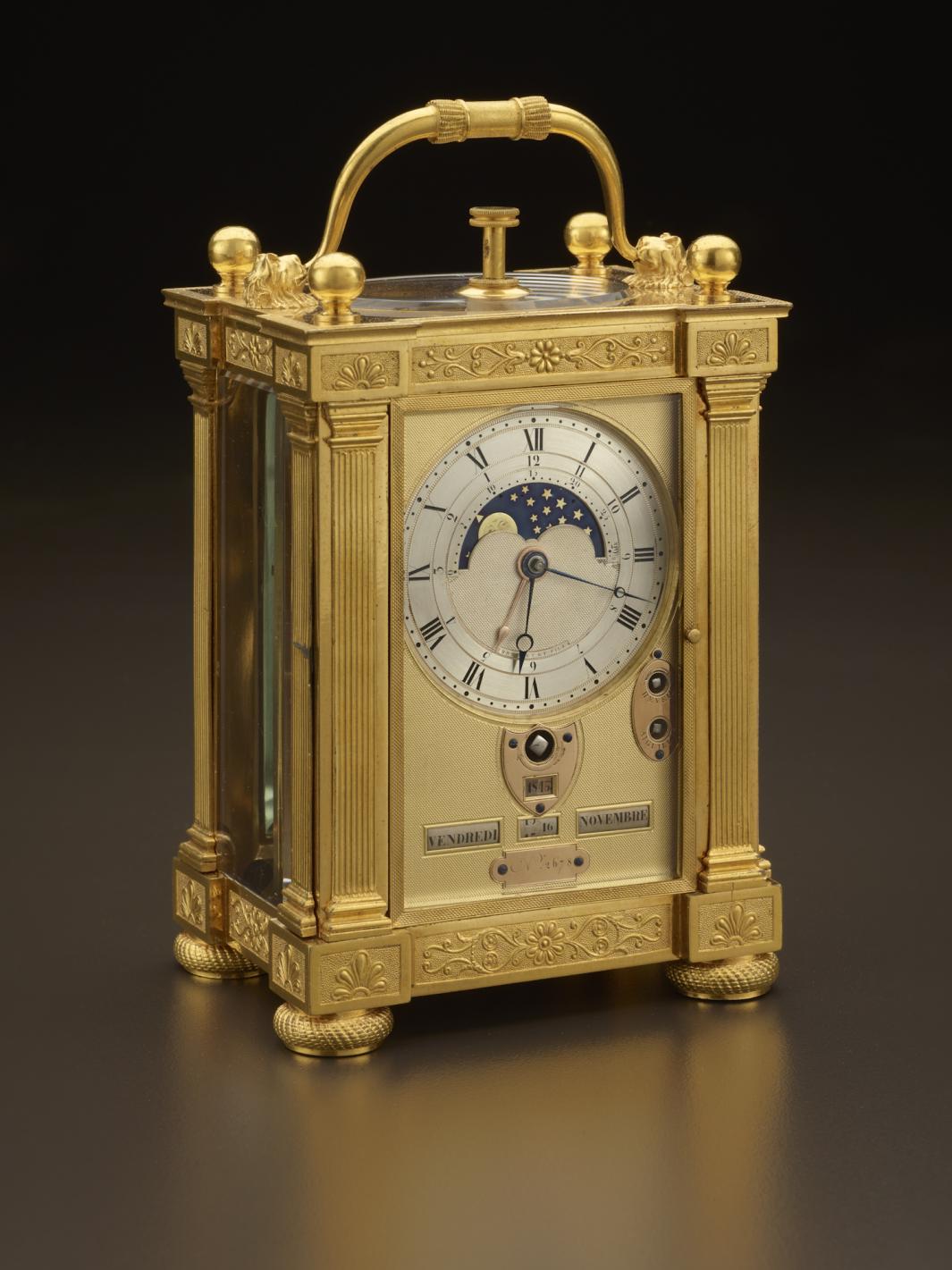 gold carriage clock with multiple dials and handle, and depiction of  night sky