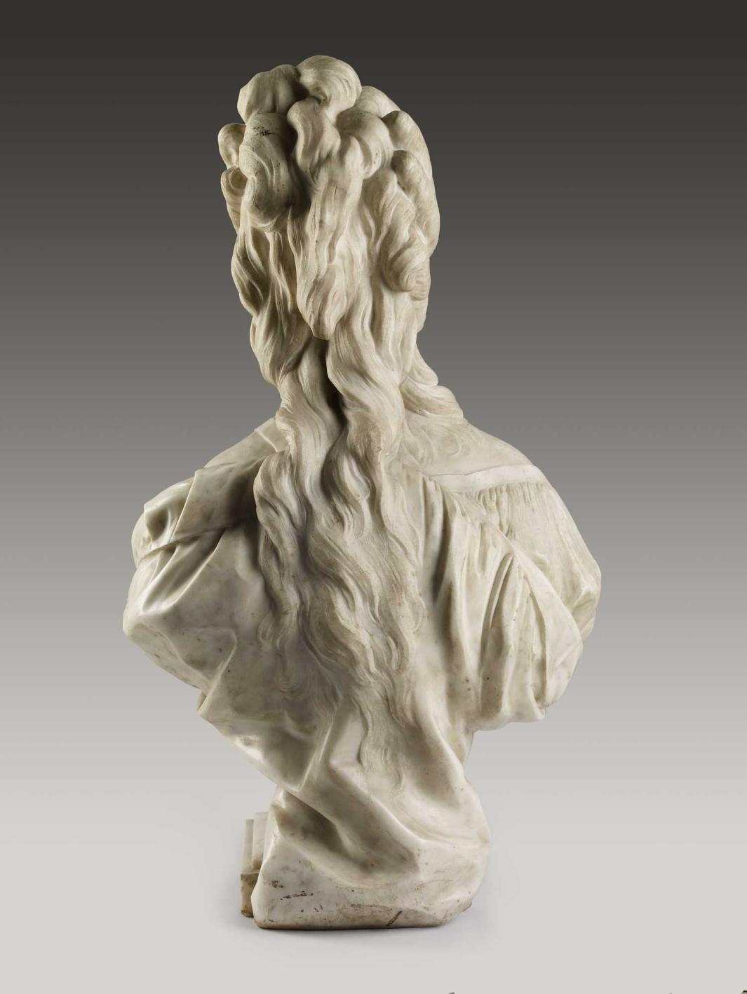Alternate view of a marble bust of a woman draped in a garment with long, curly hair.