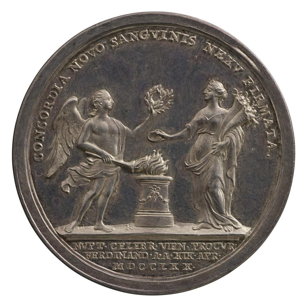Silver medal of a nude winged man holding a crown of laurel leaves in his left hand and lighting a torch from a brazier with his right hand. On the right side of the brazier, a standing woman wearing a loose, classical-style gown holds two cornucopias in her left hand 