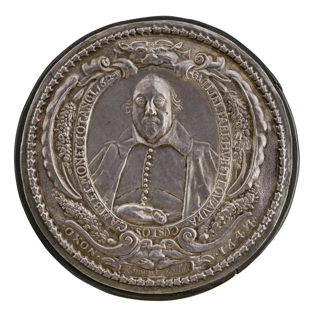 Silver portrait medal of Sir William Parkhurst framed by an ornate border of scrolls, bouquets of flowers, and vegetal motifs, with lions’ heads above and wearing a falling collar, plain buttoned doublet, and loose cloak, and holds in his hand, resting on his belly, a portrait medal (presumably of Charles I) 