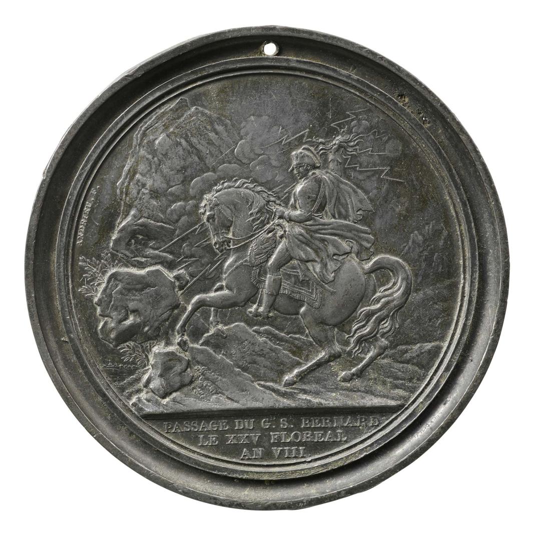 Lead medal depicting Napoleon on horseback, wearing military uniform and a commander’s cape, riding through a rocky outcrop, his right hand raised and brandishing bolts of lightning 