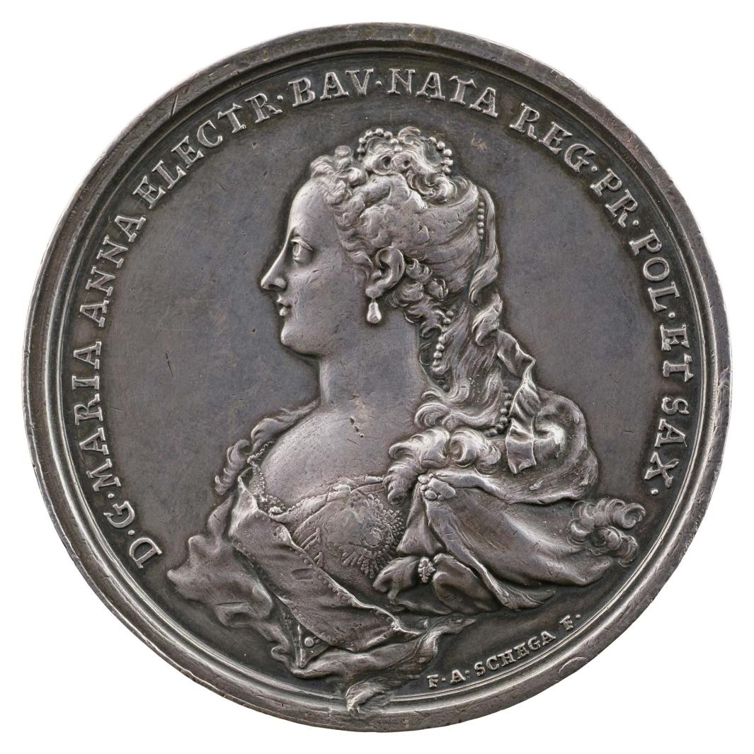 Silver medal of a woman in profile to the left wearing earrings, pearl strands woven throughout her hair, and a bodice with a sash 