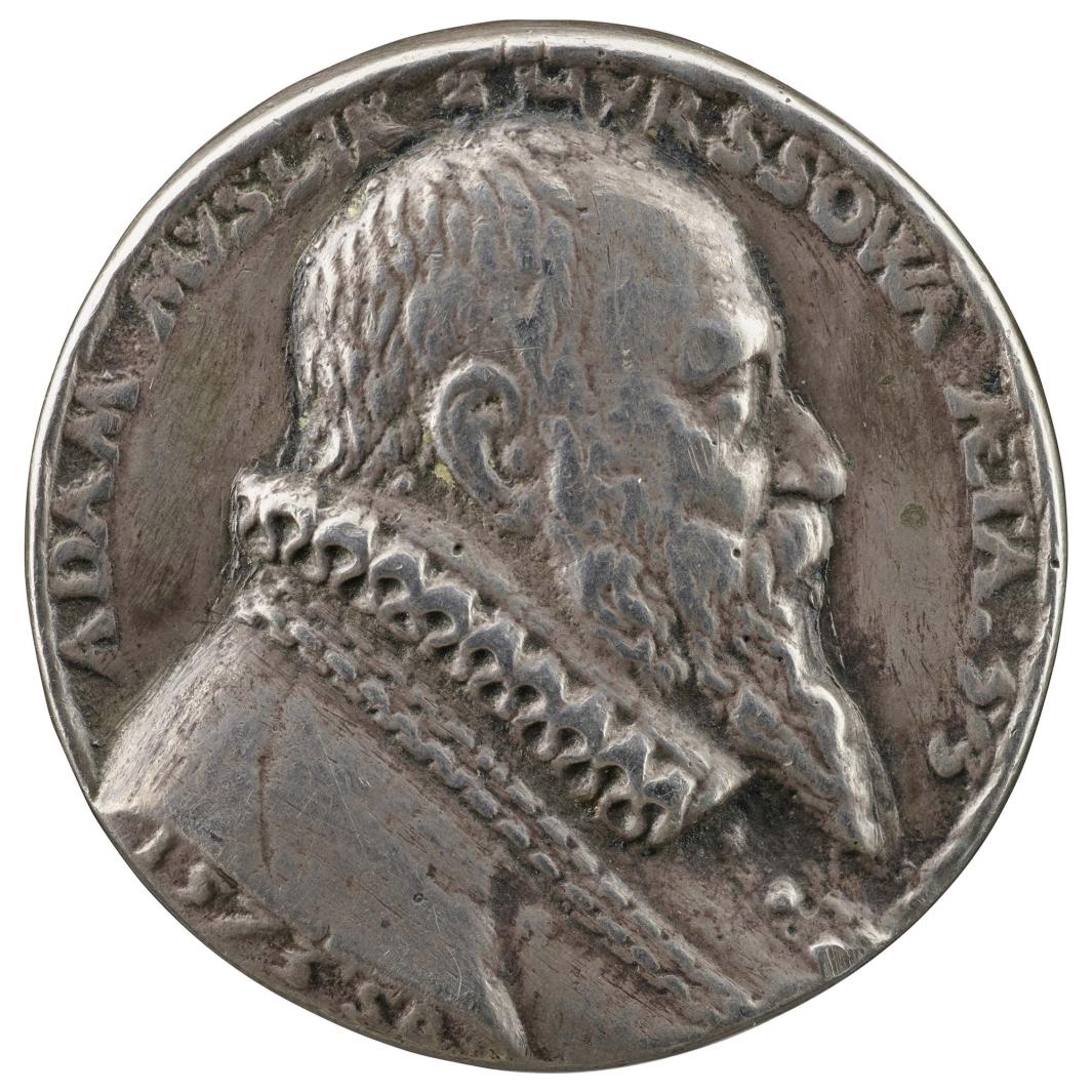 Silver medal of a man in profile to the left wearing a complex headdress