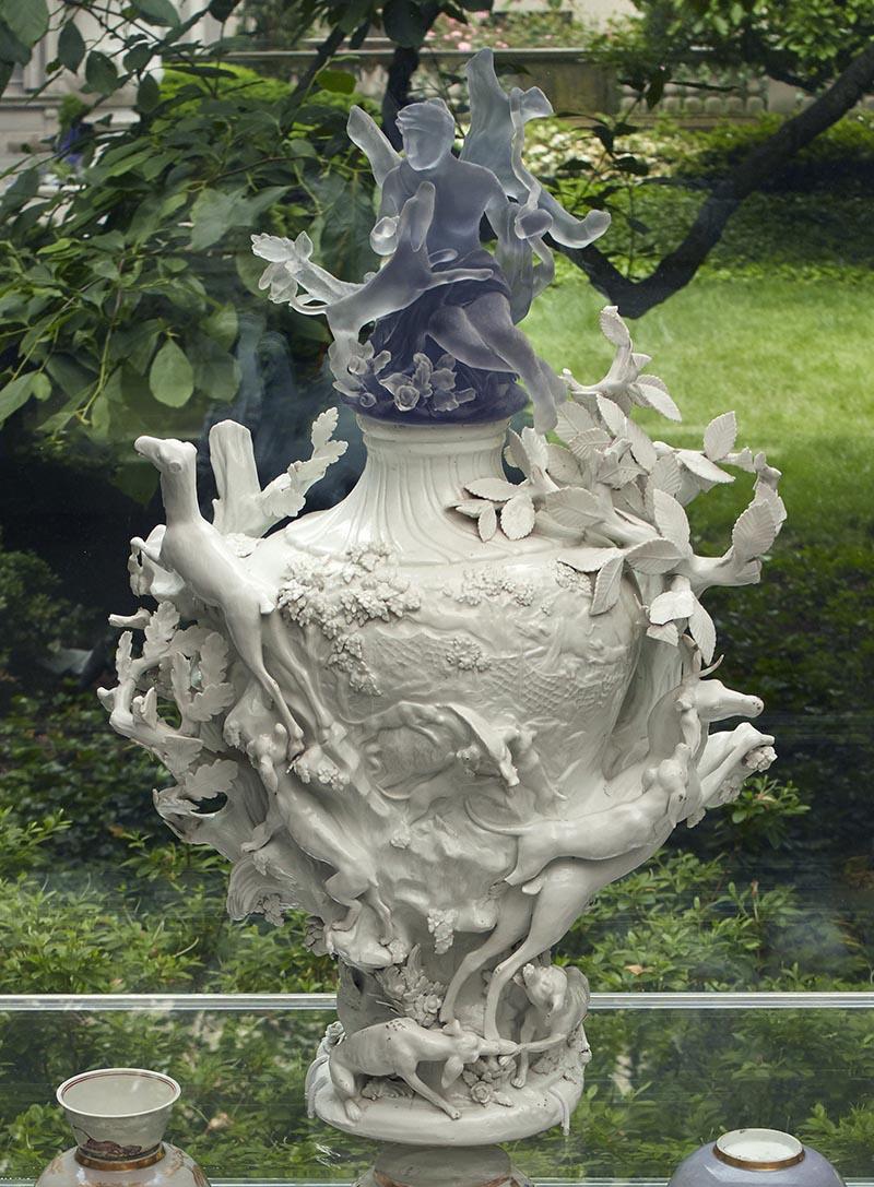 white porcelain vase molded with animals and plants, topped with blue seated female figure