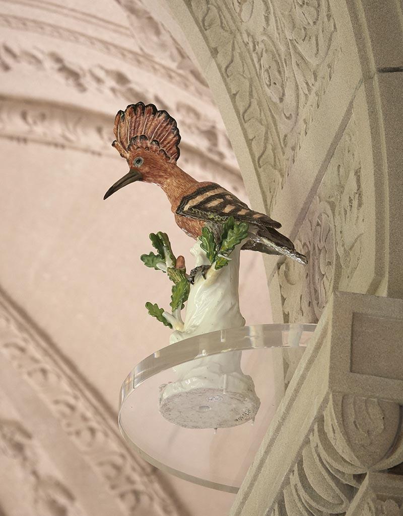 colorful porcelain bird with plume,  perched atop tree