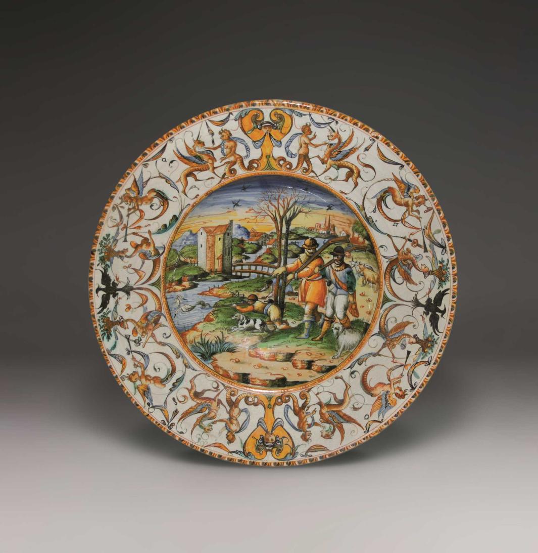 Earthenware platter with a landscape scene at the center with three figures hunting and a design of mythical creatures on the outside.