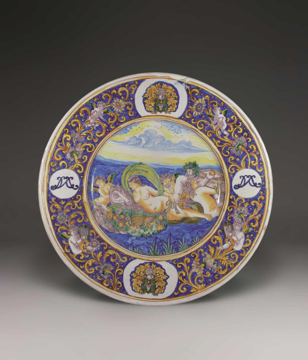 Earthenware dish with a scene of three nude figures, three winged figure, and a horse in a body of water at the center with a floral design an more winged figures on the outside. 