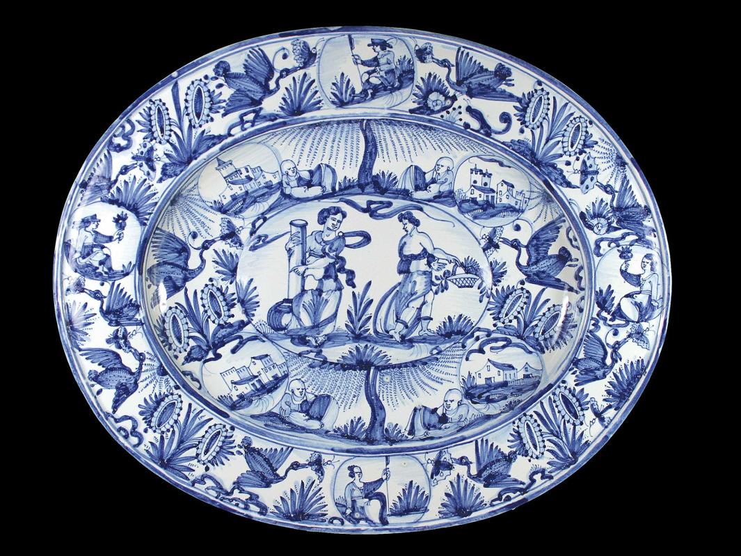 Earthenware dish in blue and white with two large figure at the center surrounded by two rings of smaller scenes as well as plants and birds.