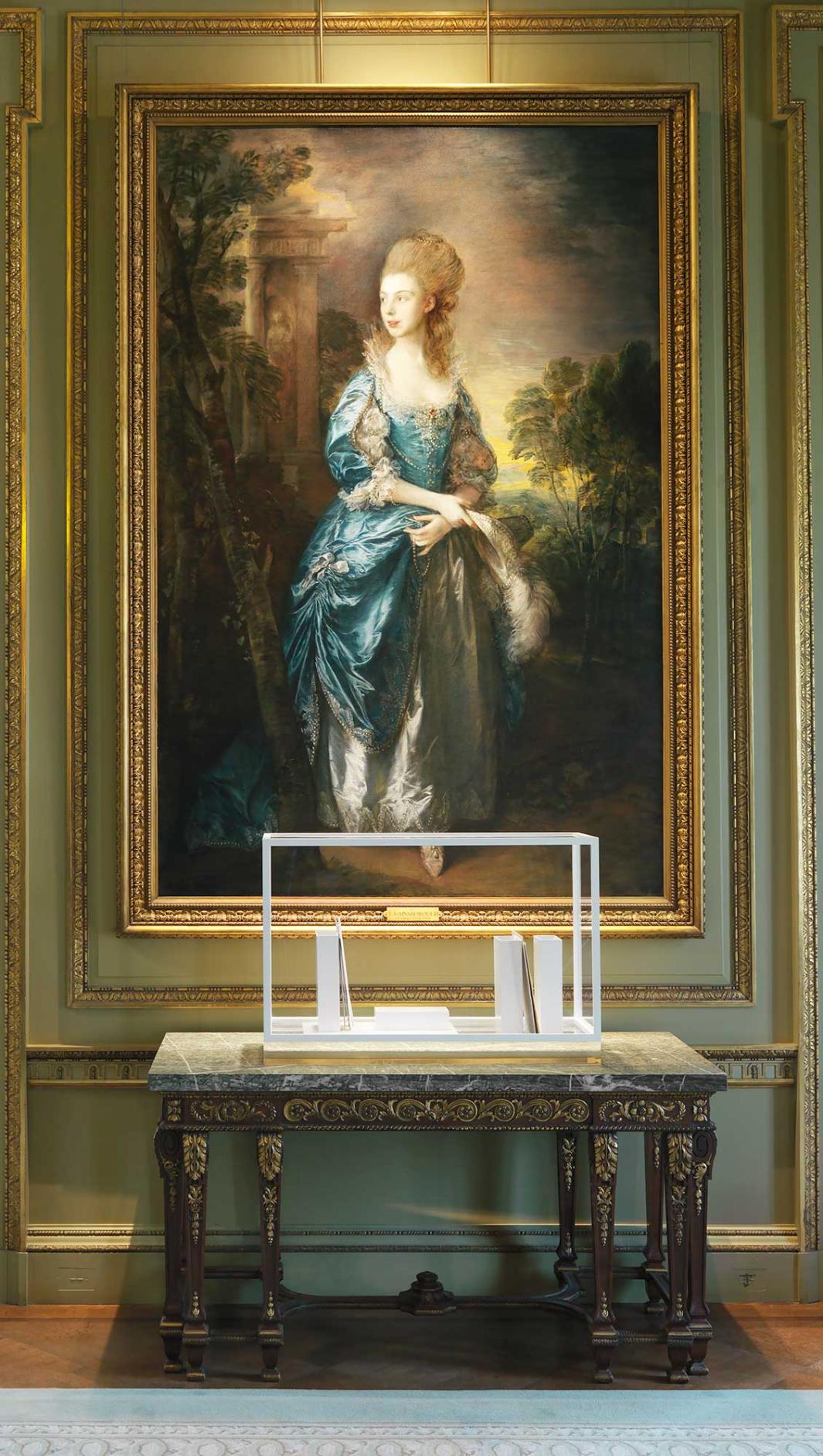 Vitrine containing white porcelain vessels, steel and gold against a full length portrait of a lady in the background