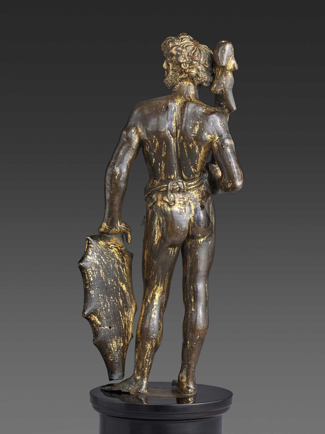 Bronze statuette of a man holding a shield and a club, as seen from the back.