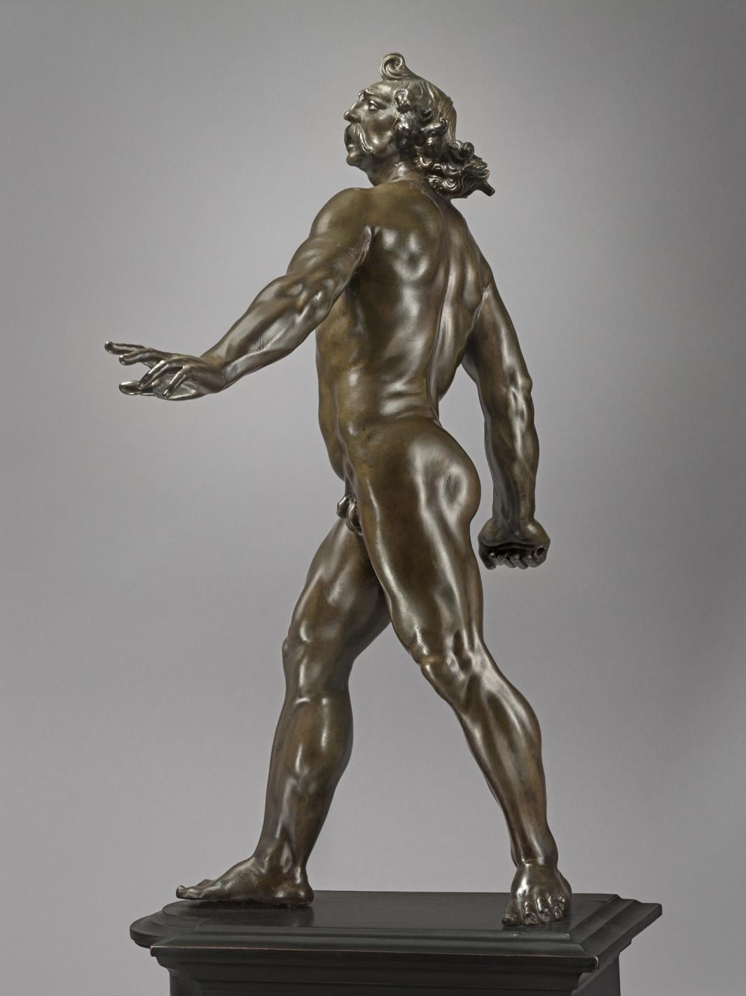 Bronze statue of man striding forward, side view.