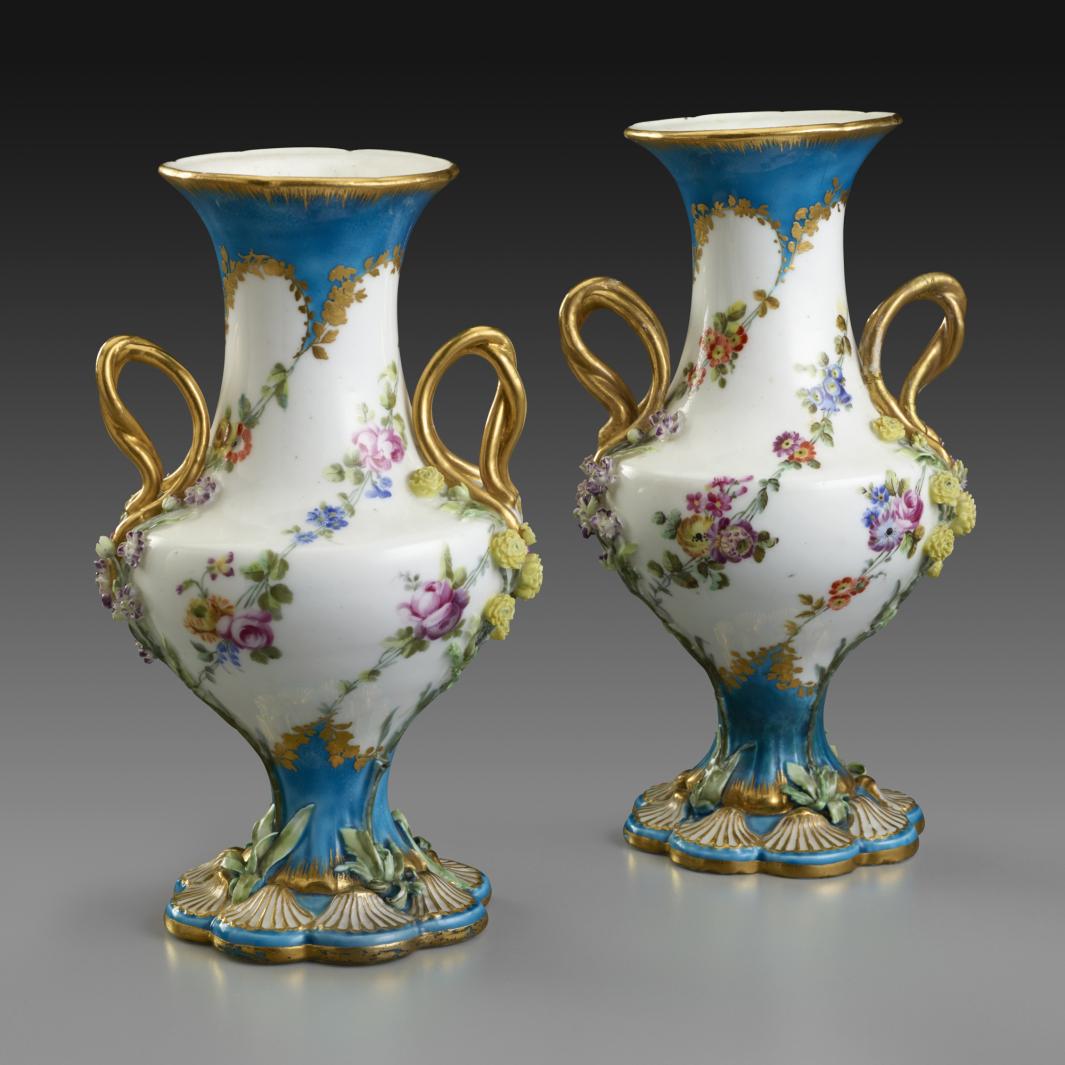 pair of small white vases decorated with floral designs and trimmed with blue and gold, with gold handles
