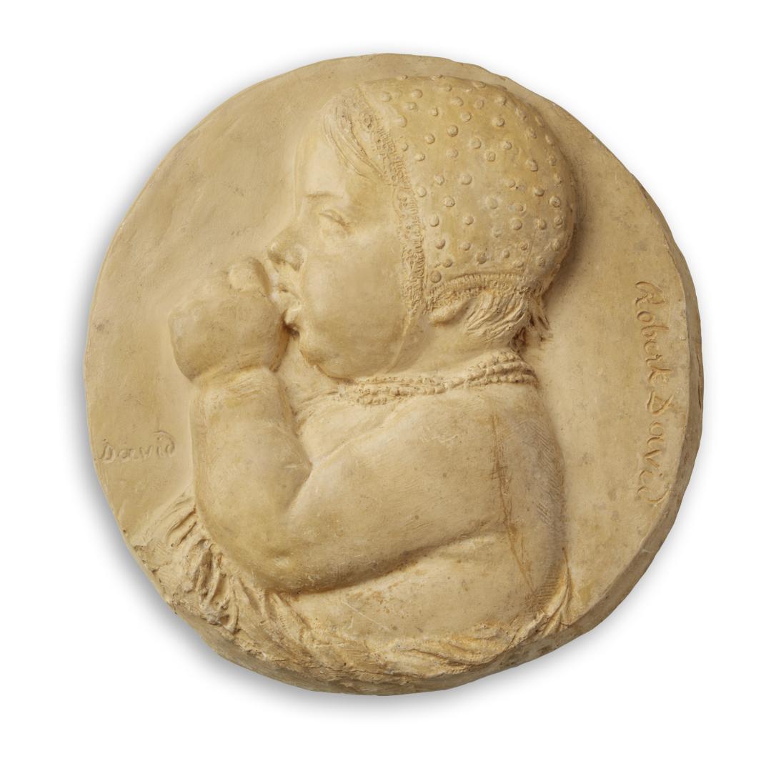 plaster carving of young child sucking thumb, atop circular plaster background