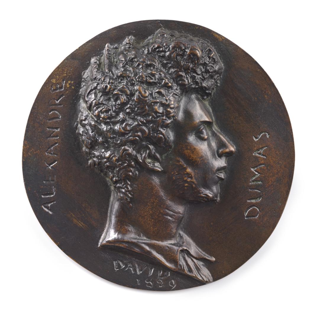 bronze of head of man in profile with curly hair atop circle of bronze with writing
