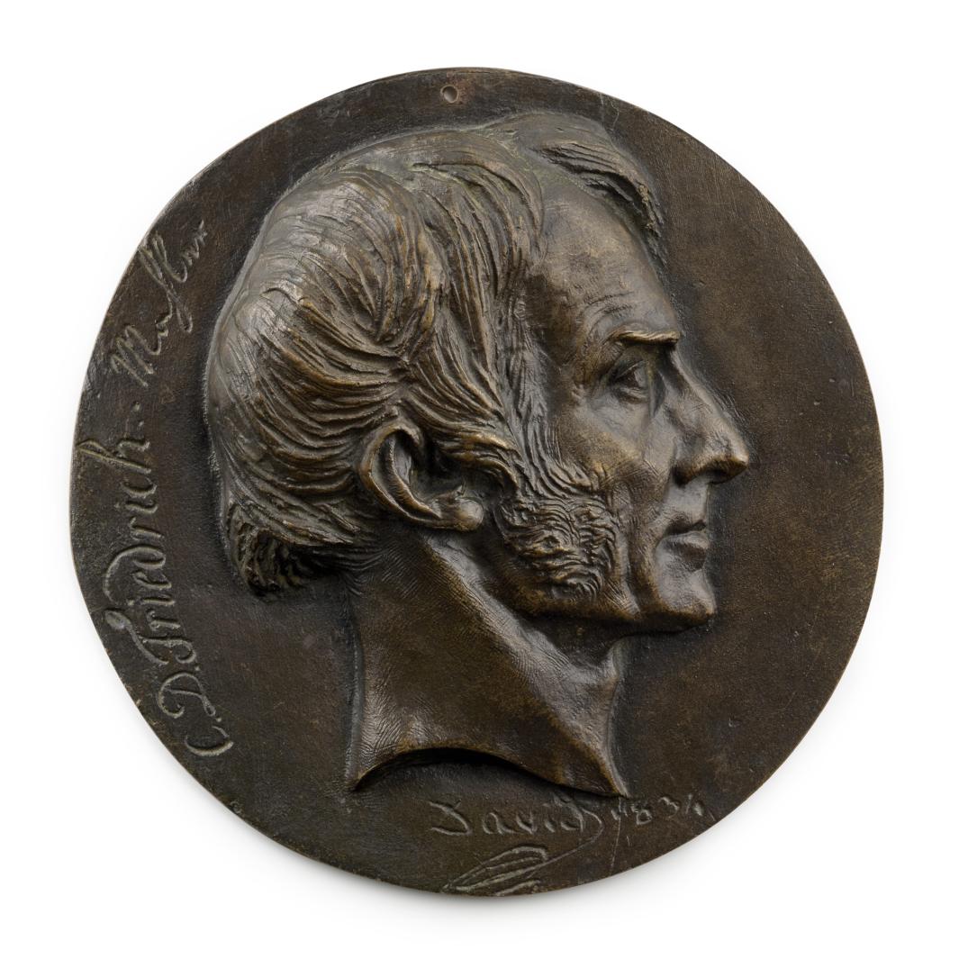 bronze head of man in profile with sideburns, atop circle of bronze with writing