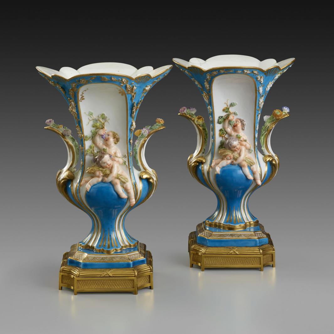 Two porcelain footed vases decorated with blue and gold featuring putti eating grapes