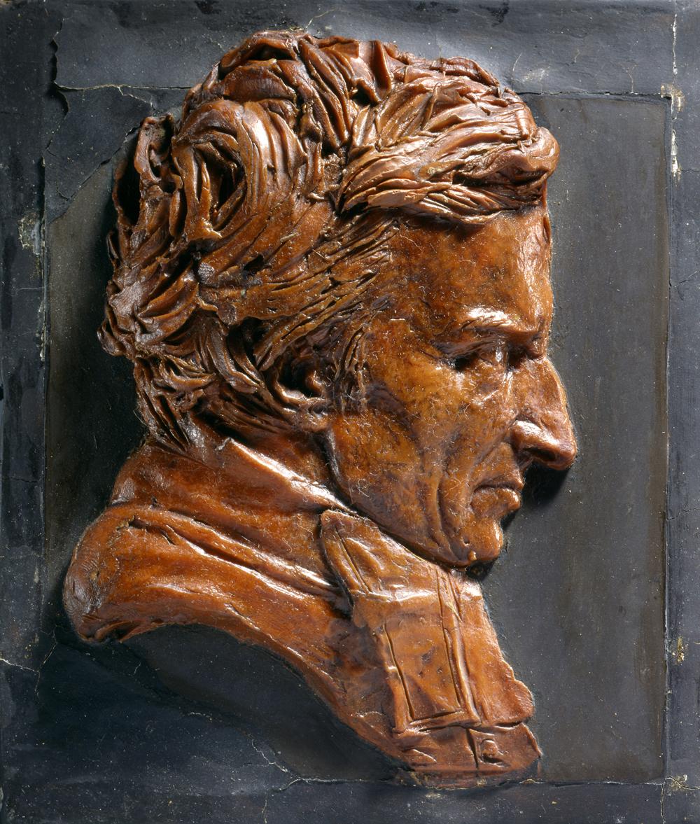 sculpted brown wax bust of man in profile, against slate background