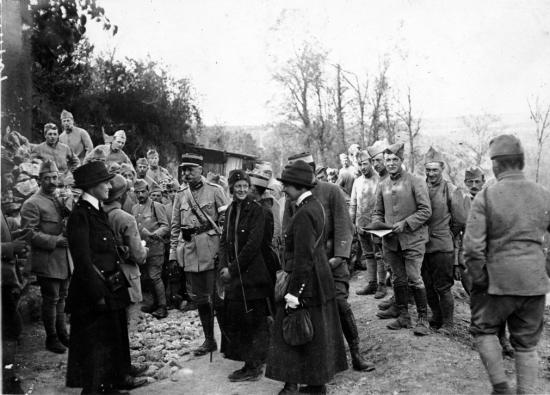 Black-and-white photo of three women surrounded by dozens of World War I soldiers in uniform on a field