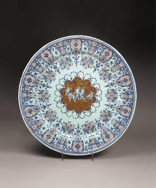 Earthenware platter with four nude figures in the middle surrounded by floral designs in blue and orange