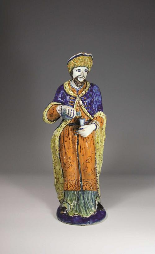 Earthenware pitcher in the shape of a bearded man in orange, blue, and yellow robes and a yellow hat.