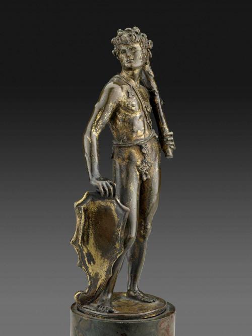 Bronze sculpture of a man standing upright.  His head is turned to his right and he is holding a club in his left hand.  A shield sits by his right leg and is underneath his right hand.