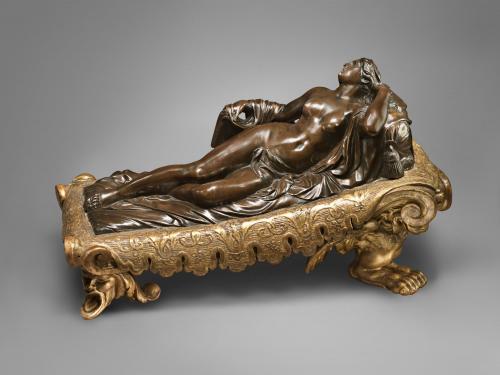 Bronze sculpture of a reclining female nude on a bed.