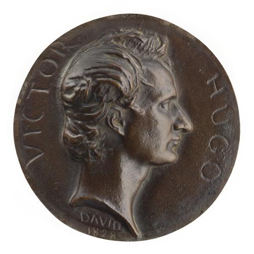 bronze head of man with thick hair in profile, atop circle of bronze with writing